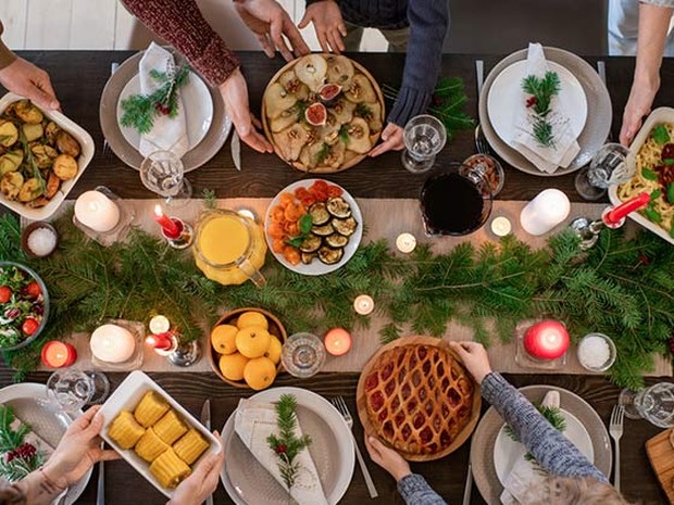 Plano cenital de una mesa decorada por Navidad con personas pasándose platos de comida