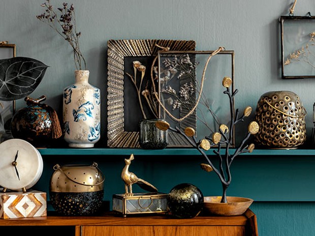Accesorios de decoración vintage en una balda de madera azul verdosa y un mueble de madera. Hay marcos de fotos, jarrones, esculturas de plantas...
