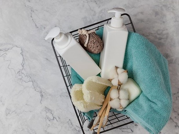 Cesta de metal negra con productos como geles, cremas y esponjas y una toalla azul clarita