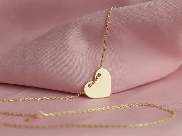 Tela de terciopelo rosa palo que hace un relieve como de ola. Por encima hay un colgante dorado de un corazón