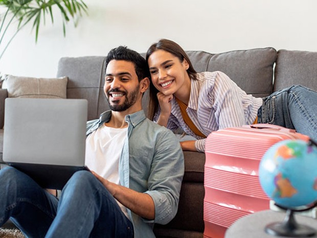 chico y chica planeando un viaje en el sofá con un portátil