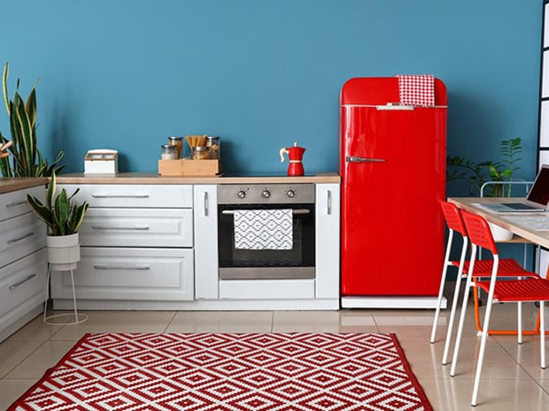 Cocina con muebles blancos y de madera, una alfombra geométrica blanca y roja y un frigorífico rojo estilo retro