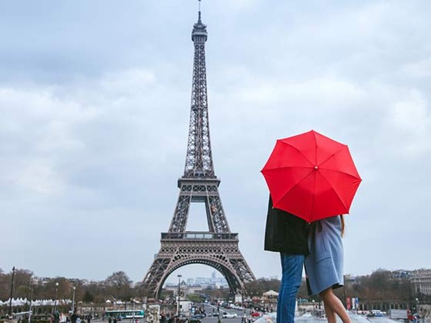 Pareja escondidos tras un paraguas rojo observando la Torre Eiffel en un día nublado