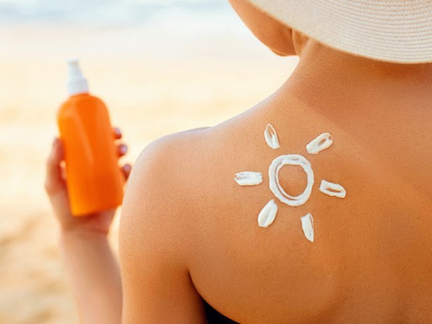 Espalda de mujer con un tono de bronceado y un sol dibujado con crema solar. En la mano sostiene un bote de crema naranja.