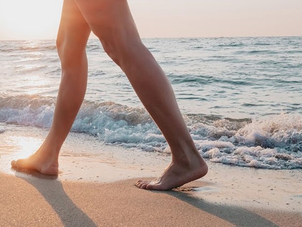 Piernas de una mujer caminando por la orilla de la playa con una luz de atardecer