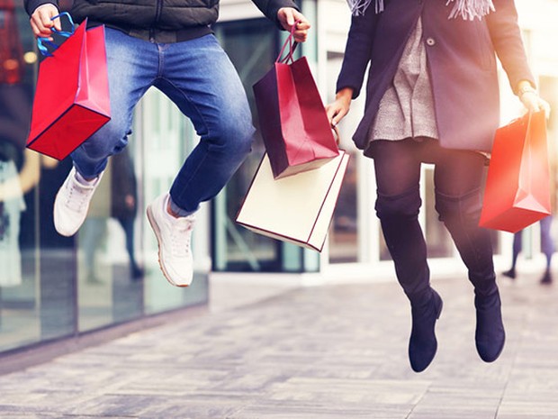 Plano de cintura para abajo de una chica y un chico saltando con bolsas de compras en las manos