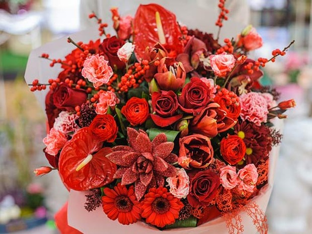 Ramo de distintas flores en tonos rojos. Lo está sujetando una persona que no vemos.