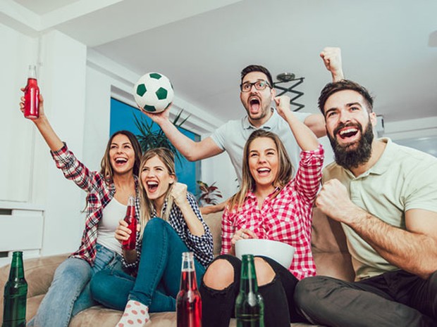 Grupo de amigos con cervezas celebrando un gol en el sofá de casa