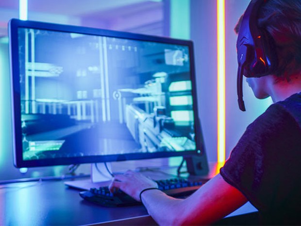 Chico joven con cascos inalámbricos de gamer con micrófono jugando a un vídeojuego en el ordenador