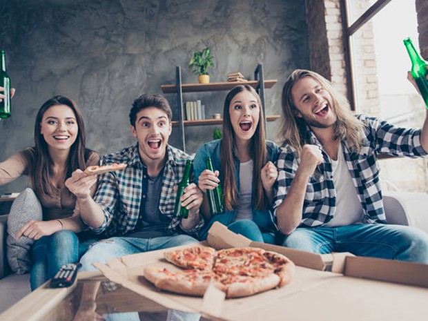 Grupo de amigos viendo un partido de fútbol con pizzas y cervezas