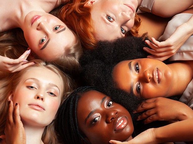 5 mujeres tumbadas en círculo con las cabezas tocándose. Cada una tiene un tono de piel diferente.