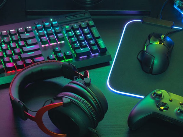 Auriculares de gamer negros y rojos, joystick negro, ratón de gamer negro y teclado de gamer con las teclas iluminadas de colores