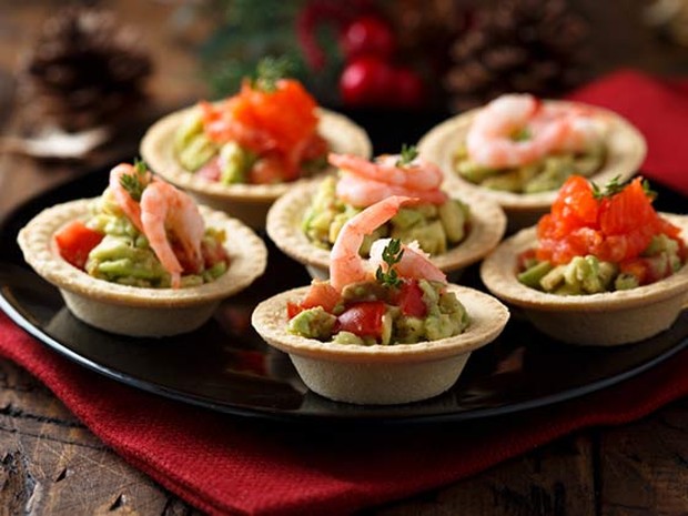 Aperitivos de aguacate, tomate cherry y langostinos en una mesa de madera con decoración navideña