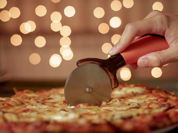 Persona cortando una pizza con un corta pizzas y unas luces de fondo