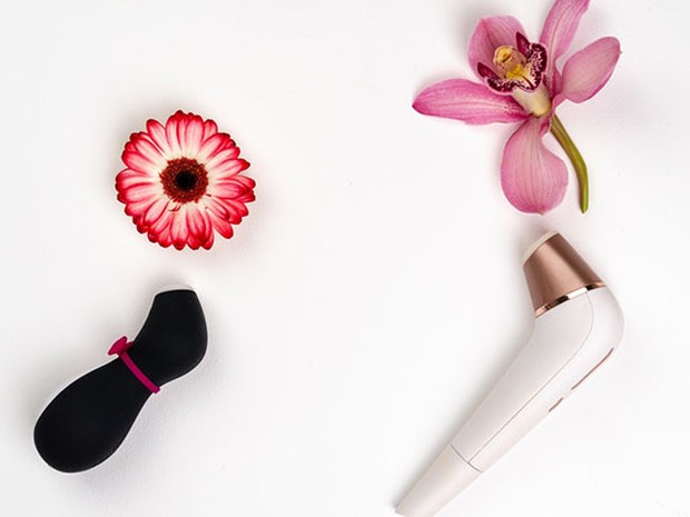Satisfyer penguin negro y rosa debajo de una flor roja y satisfyer blanco y dorado debajo de una flor rosa. Todo sobre un fondo blanco.