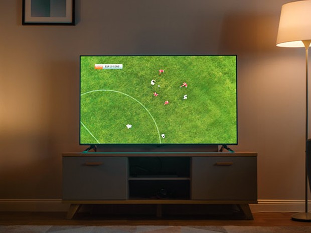 Televisión plana con un partido de fútbol en un salón con luz tenue