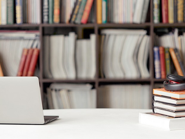 Biblioteca donde hay una mesa con libros y un ordenador portátil