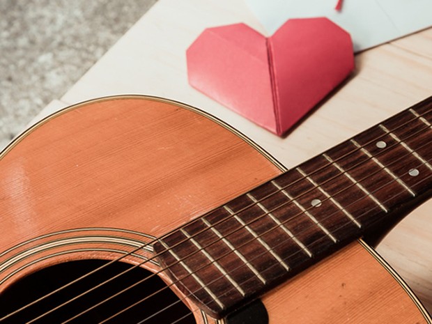 Guitarra sobre una mesa donde se encuentra también un corazón de papiroflexia en color rojo