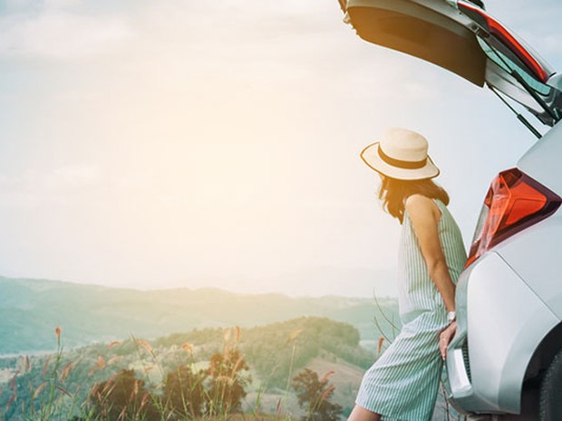 Chica contemplando un paisaje apoyada en el maletero de un coche