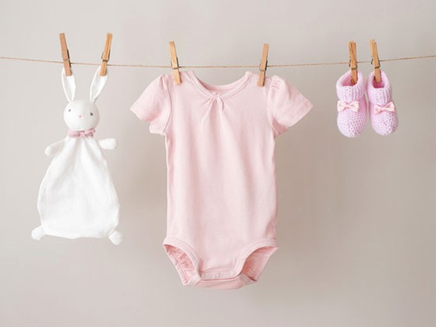 Bodie rosa de bebé, zapatos y peluche tendidos en una cuerda con pinzas
