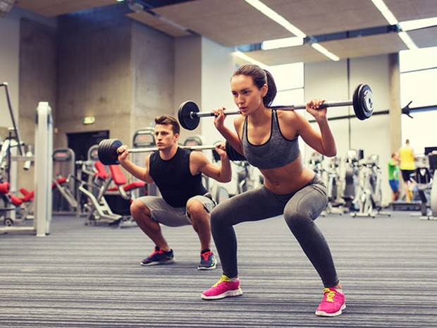 Chica joven y chico joven haciendo sentadillas en el gimnasio con barras de pesas