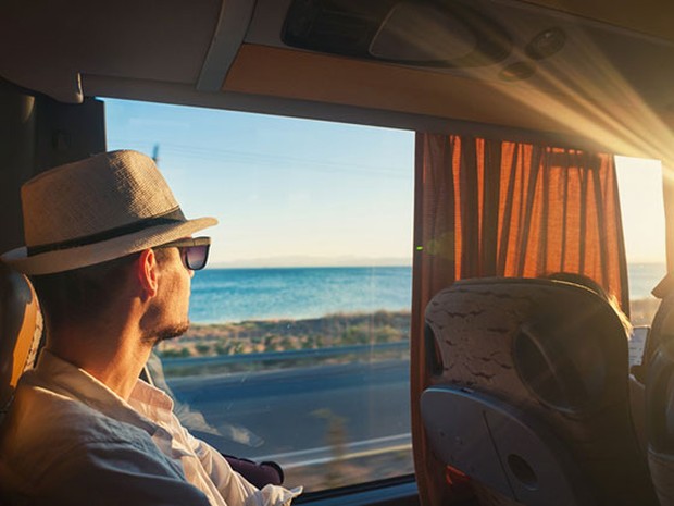 Hombre joven sentado en un autobús mirando el mar por la ventana