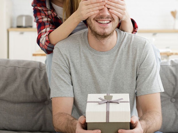 Chica tapando los ojos a un chico con un regalo en sus manos
