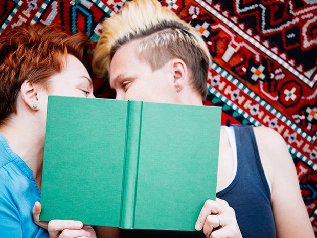 Pareja de mujeres jóvenes mirándose detrás de un libro verde.
