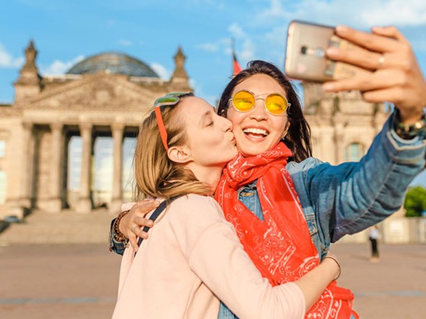 Pareja de dos mujeres jóvenes haciéndose un selfie frente a un monumento