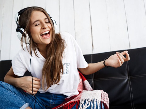 Chica joven con el pelo largo, y vestida con una camiseta blanca de manga corta y vaqueros, sentada escuchando música con auriculares de diadema blancos