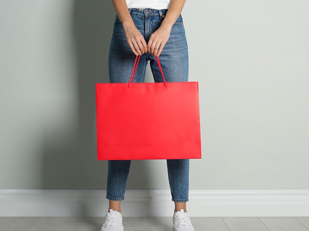 Vemos a una chica de cintura para abajo vistiendo unos vaqueros y sujetando una bolsa de papel roja