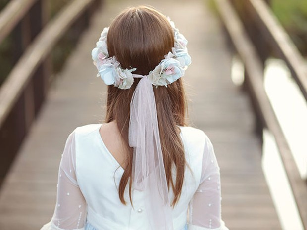 Niña vestida de comunión que está de espaldas y tiene el pelo liso y suelto con una diadema de flores blancas y rosas palo