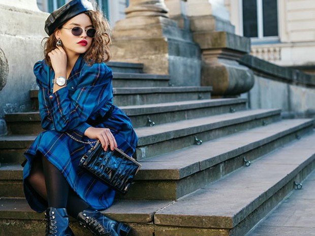 Mujer joven vestida con un abrigo tartan azul sentada en unas escaleras de piedra