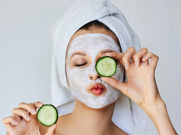 Chica jóven con una mascarilla facial y rodajas de pepinillos