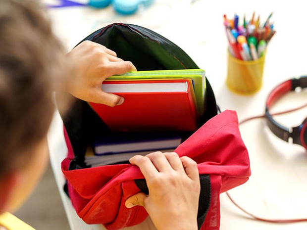 Niño metiendo unos libros rojos y verdes en su mochila escolar roja