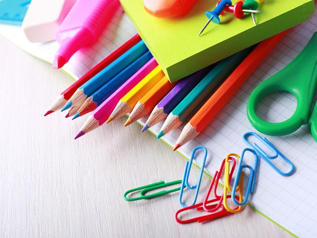 Artículos de papelería escolar sobre una mesa de madera blanca. Hay lápices, subrayadores, tijeras, post-its, clips...