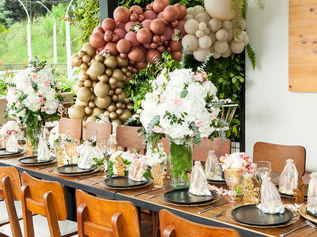 Mesa decorada de comunión. Hay platos negros, ramos de flores rosas y un arco de globos rosas, beige y blancos