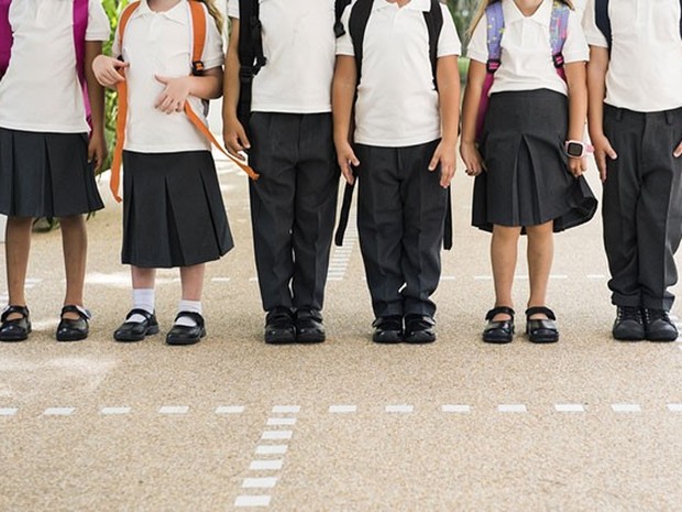 Niños y niñas en el patio de un colegio vistiendo uniforme de falda o pantalón negro y polo blanco