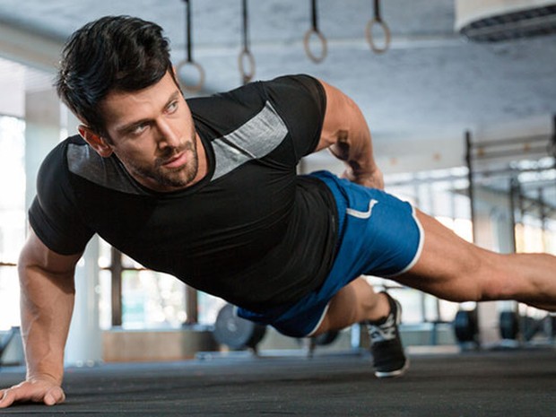 Hombre haciendo flexiones con un brazo en el gimnasio