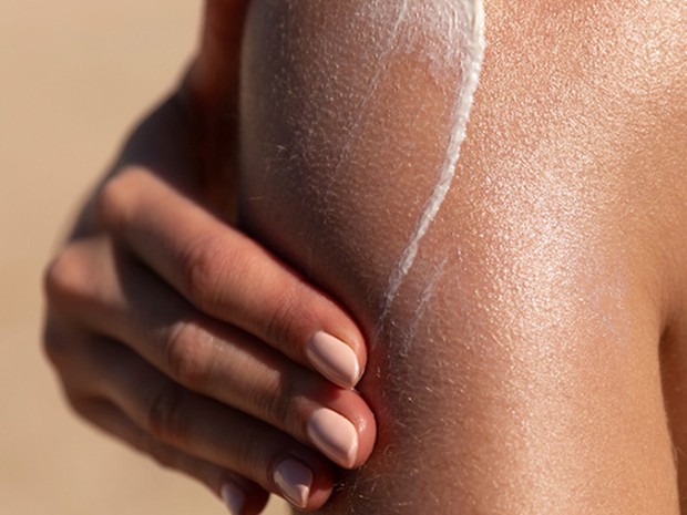 Mujer echándose crema solar sobre un hombro