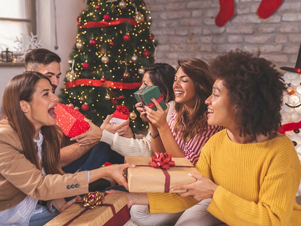 Grupo de amigos entregándose regalos junto a un árbol de navidad
