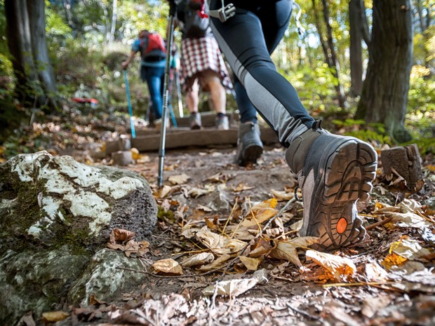 Varias personas haciendo senderismo por una ruta de bosque. En primer plano se ve una bota de montaña