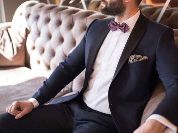 hombre vestido con traje y pajarita granate sentado en un sofá beige