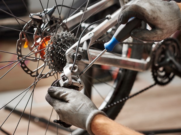 Manos con unos guantes blancos manchados de grasa de bicicleta arreglando la cadena de una rueda