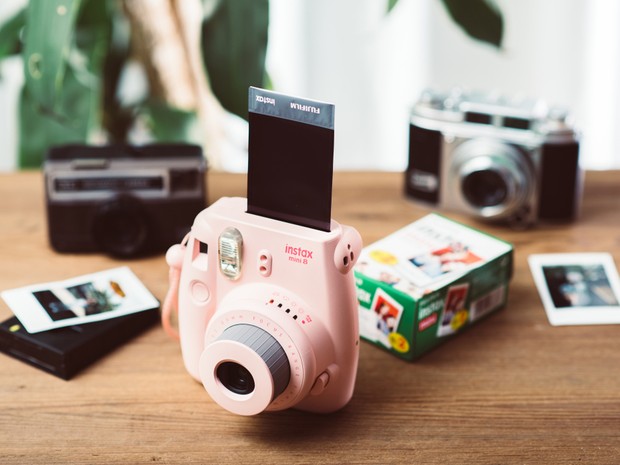 Cámara Fujifilm Instax mini 8 rosa sobre una mesa de madera. Detrás hay otras cámaras.