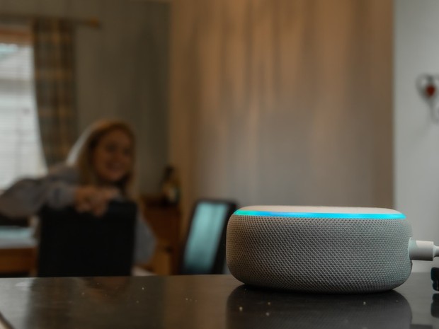 Altavoz inteligente Amazon Echo Dot en blanco con la luz azul de arriba iluminada porque se ve que al fondo una chica le está hablando