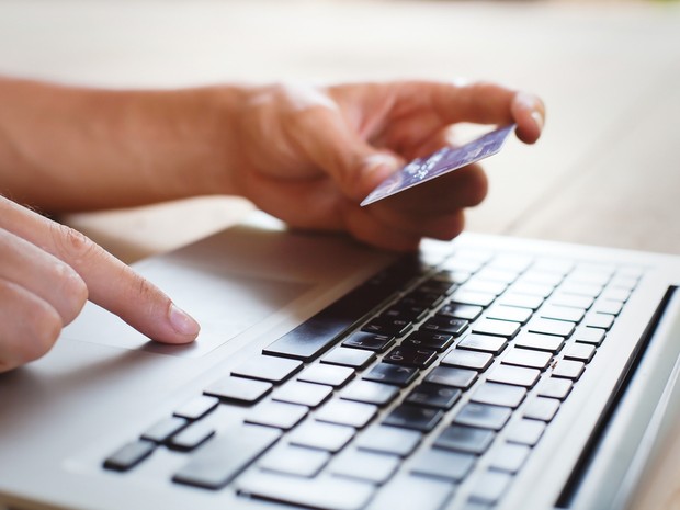 Manos de una persona utilizando su tarjeta de crédito para comprar online. Se ve también el teclado de un portátil.