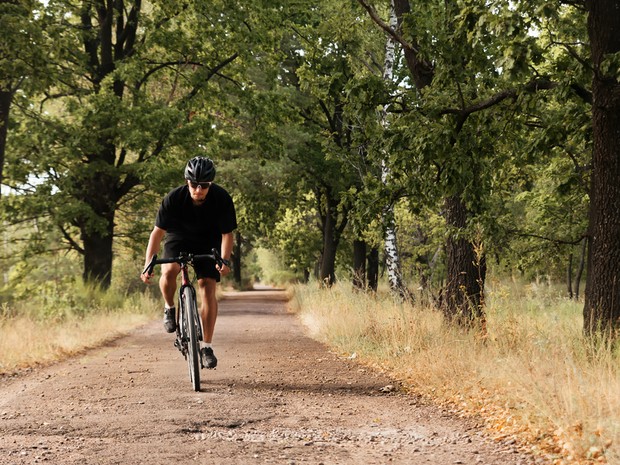 Hombre joven con una bicicleta de gravel pedalenado por un camino de tierra con árboles alrededor
