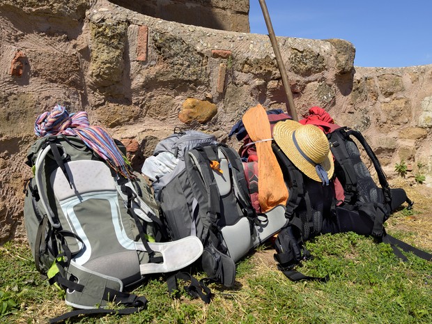 Varias mochilas de peregrino apoyadas en un muro de roca sobre el cesped verde