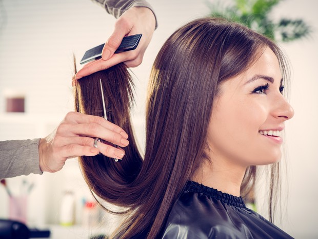 Mujer castaña sonriente mientras le cortan las puntas del pelo